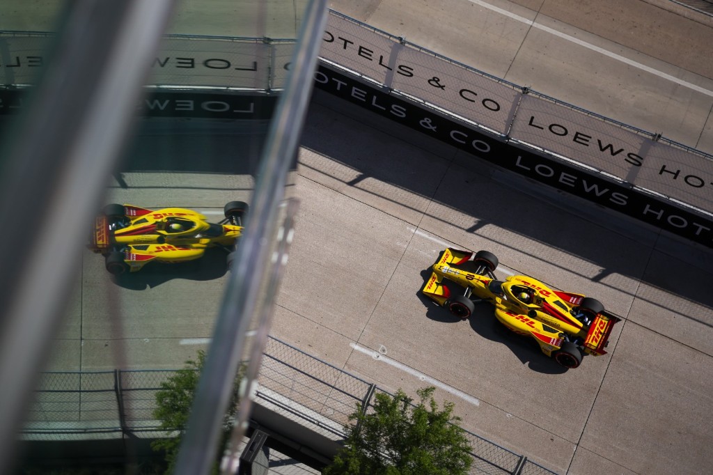 Alex Palou driving the number 10 DHL Honda IndyCar on the Arlington street circuit, with the car reflected in a glass building facade.